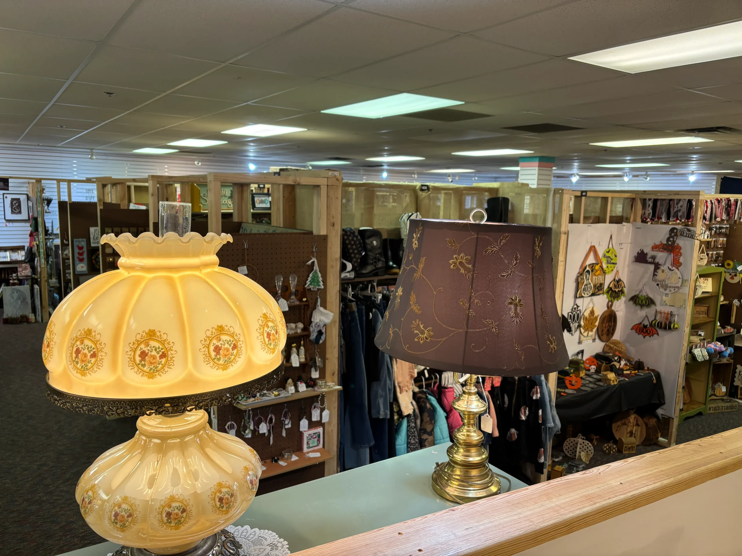 Two vintage lamps on a display table, one yellow with floral patterns and another brown with gold embroidery, overlooking a bustling market area Two vintage lamps on a display table, one yellow with floral patterns and another brown with gold embroidery, overlooking a bustling market area